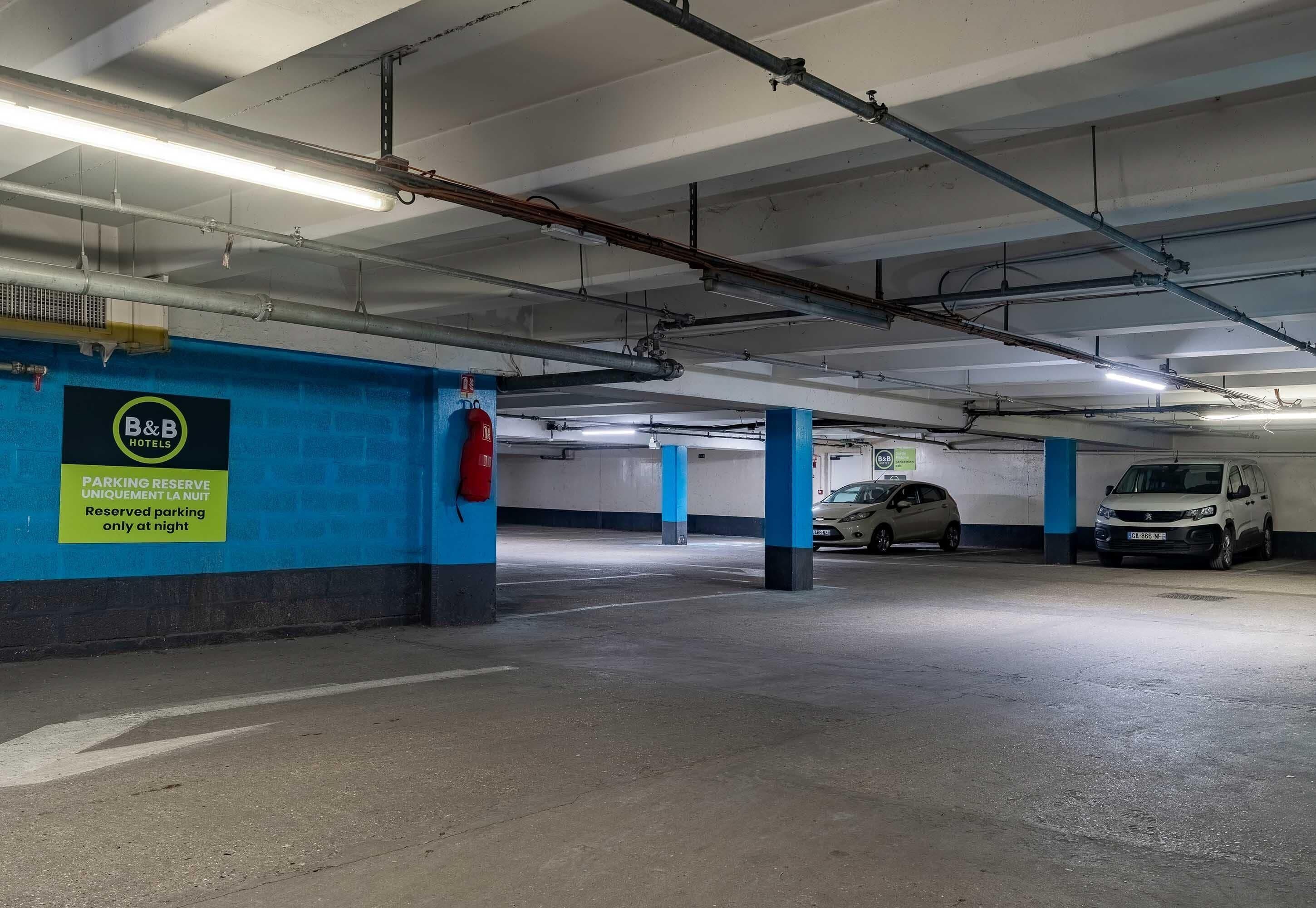 A parking garage with blue pillars, a B&B hotel sign, and reserved parking signs.