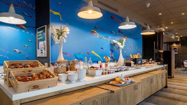 A buffet counter with wooden crates of pastries, a variety of food items, and decorative vases. - B&B Hotel Boulogne Sur Mer Centre Les Ports (Boulogne-sur-Mer)