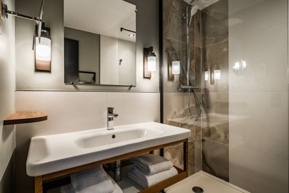 A modern bathroom with a white sink, a mirror, and a shower.
