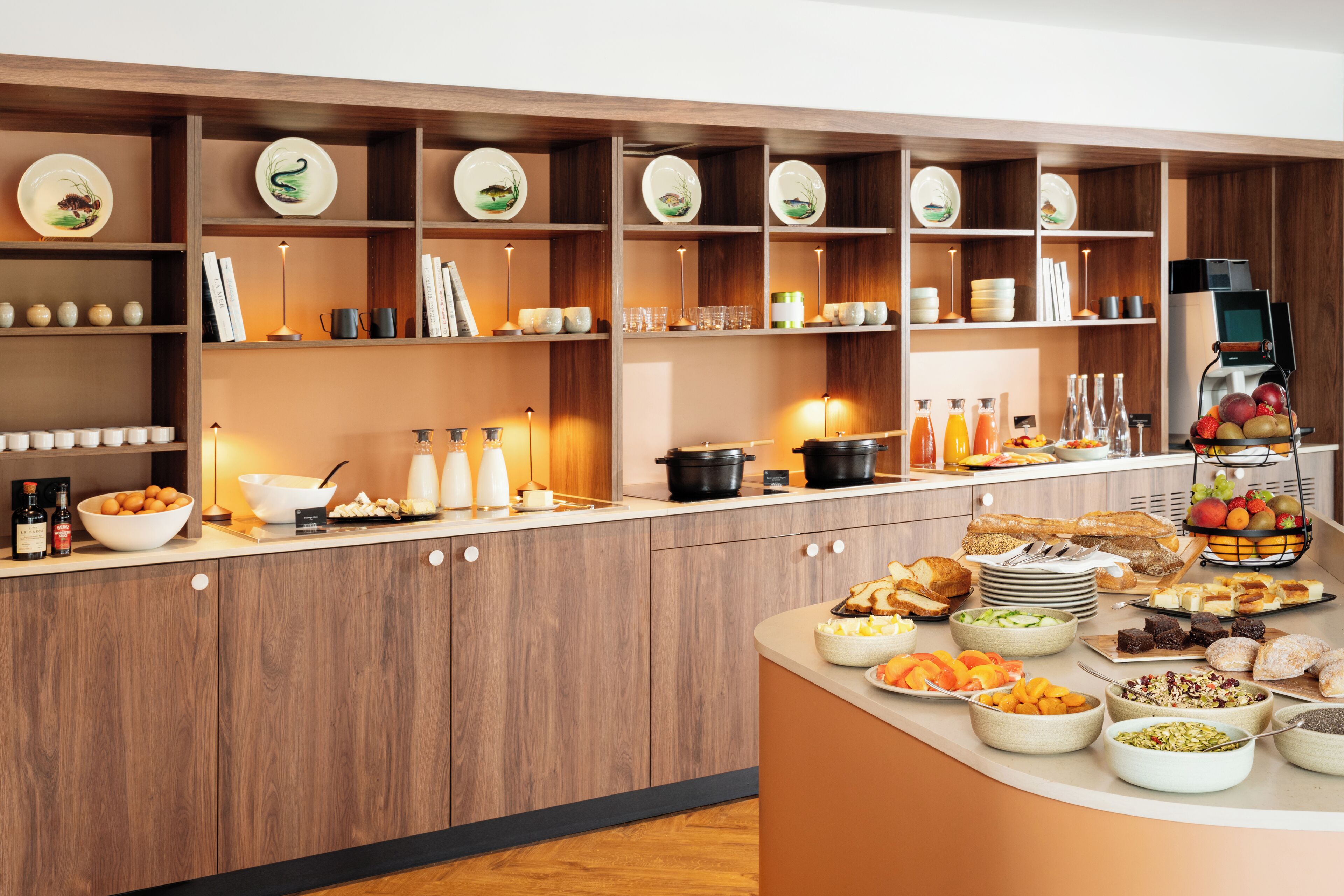 Montaje tipo bufé con diversos alimentos y bebidas, repisas de madera con platos y una máquina de café.