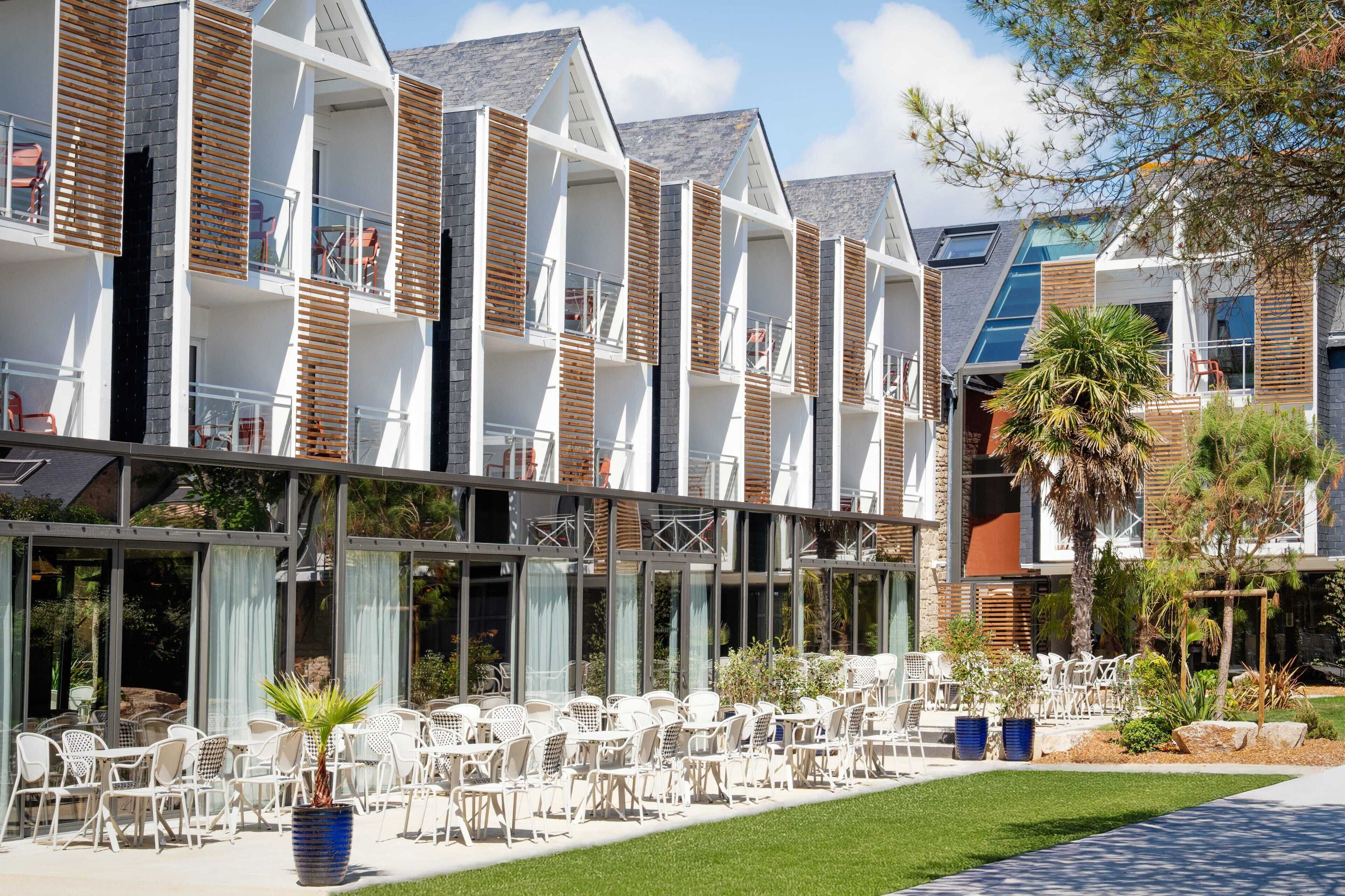 Un hotel moderno con varios balcones, mobiliario exterior y un jardín bien cuidado.