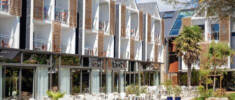 Un hotel moderno con varios balcones, mobiliario exterior y un jardín bien cuidado.