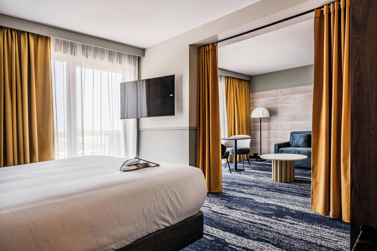 A hotel room with a large bed, a flat-screen TV, a desk with a chair, and a sofa.