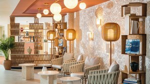 Un interior moderno con muebles de mimbre, un muro estampado y una estantería con libros y adornos.