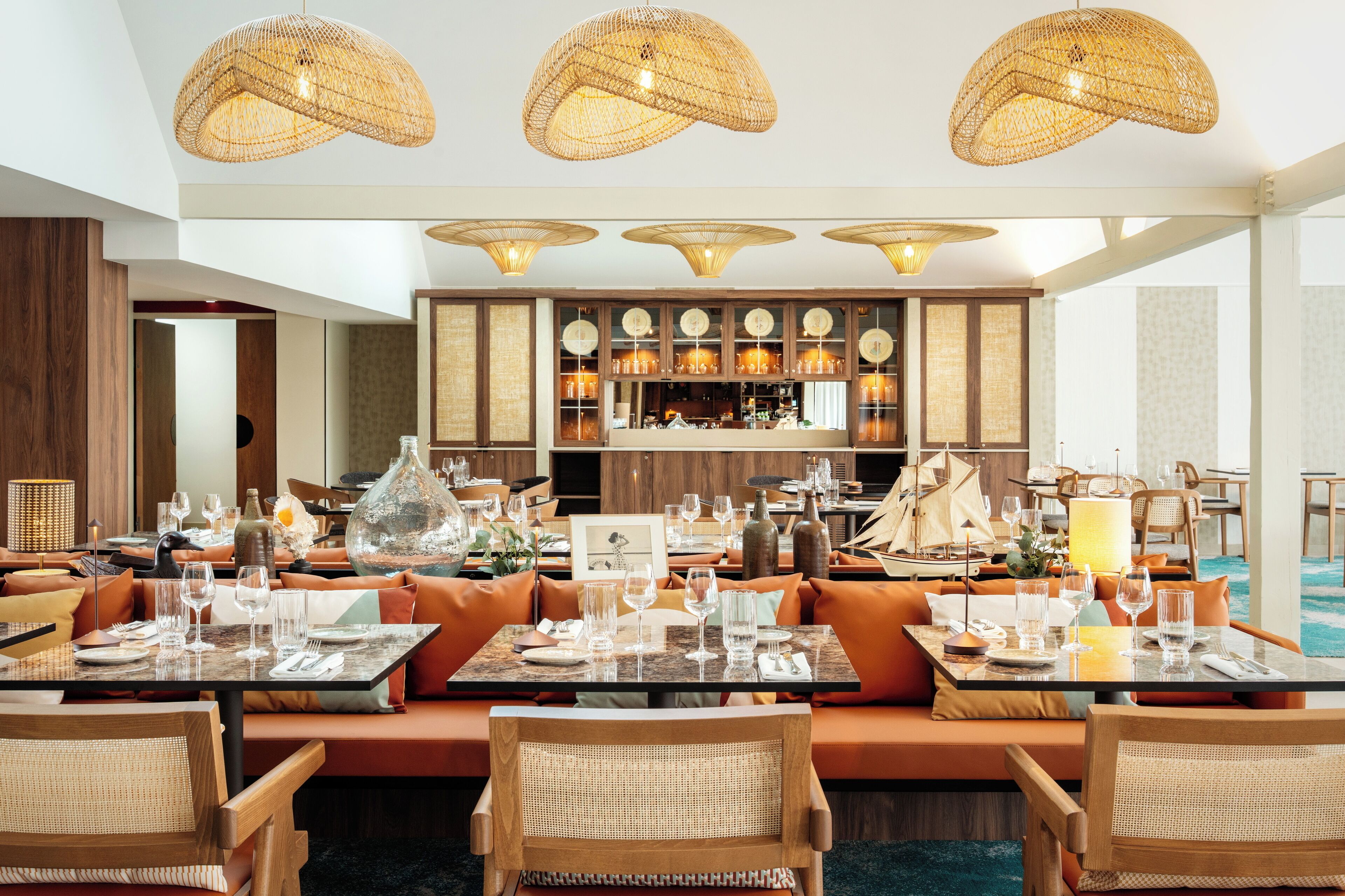 A restaurant with multiple dining tables, wicker ceiling lamps, and a bar area with wooden cabinets.