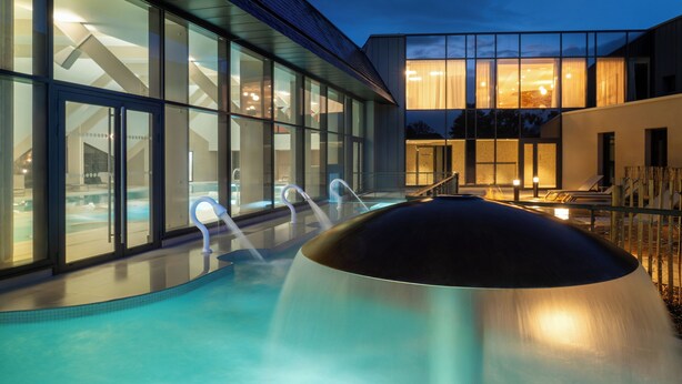 Un área de piscina moderna al aire libre con paredes de vidrio transparente, un jacuzzi y una zona de estar bien iluminada.