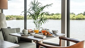 Una mesa de comedor con alimentos para el desayuno, una planta y vista a un lago.