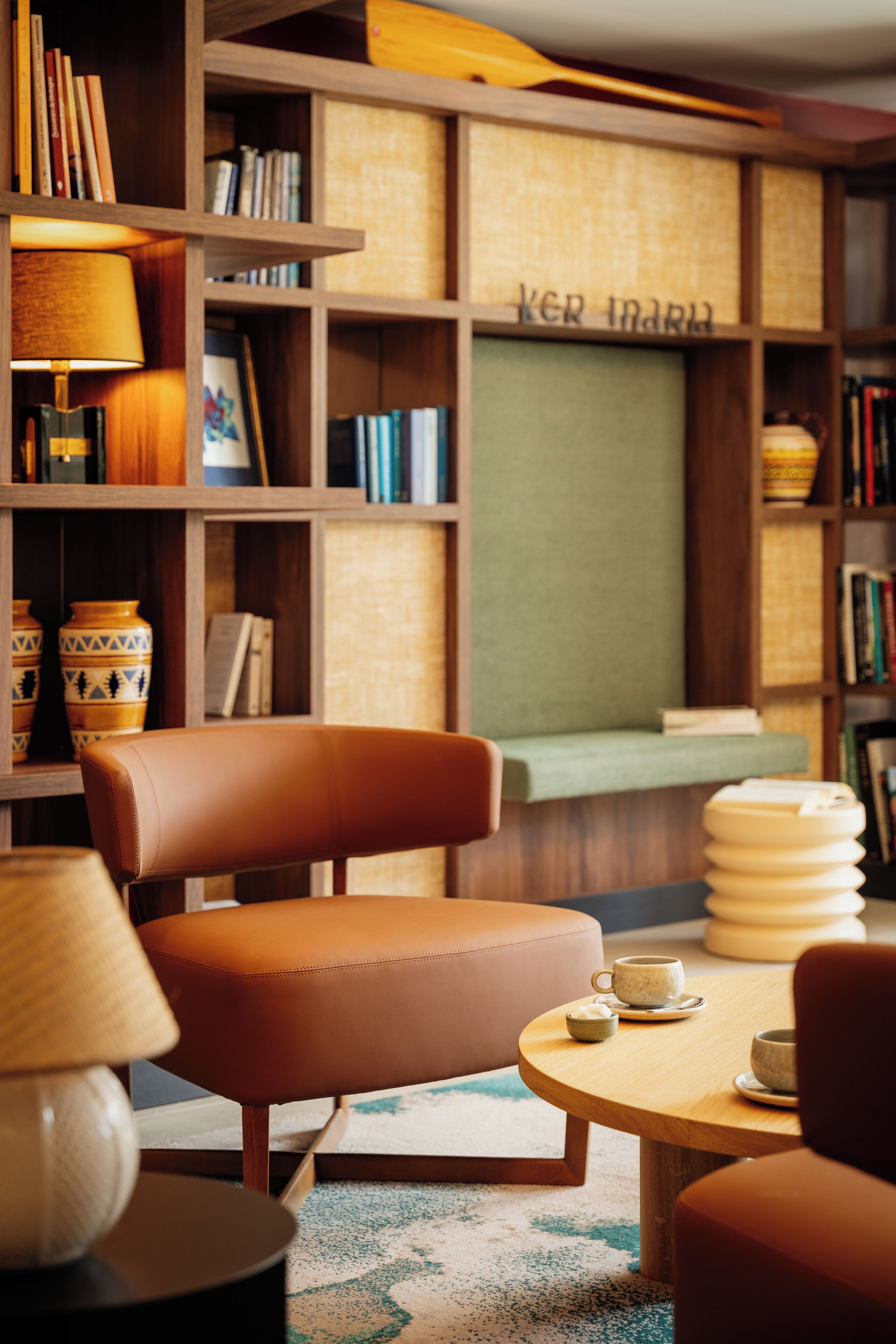 Un rincón de lectura acogedor con un sillón de cuero, una mesita redonda con una tetera y una estantería llena de libros y objetos decorativos.