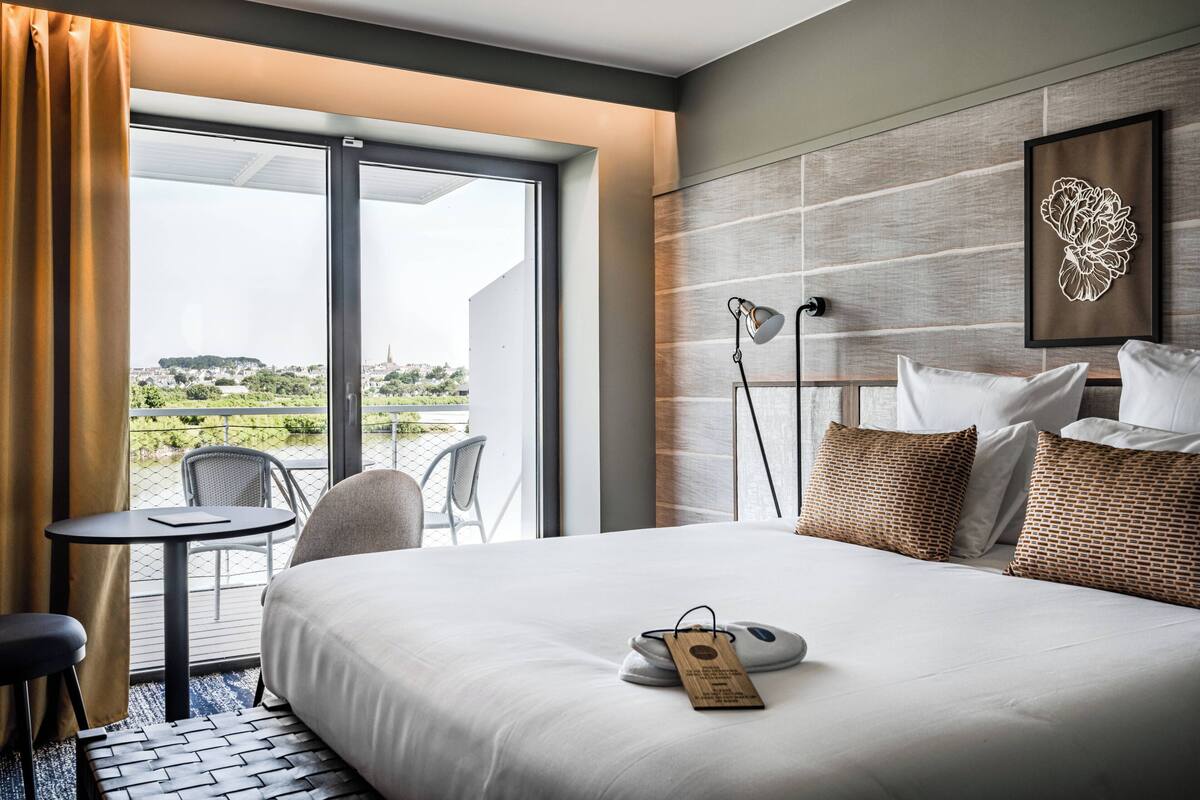 A hotel room with a bed, a desk, a chair, a table, and a view of the cityscape.