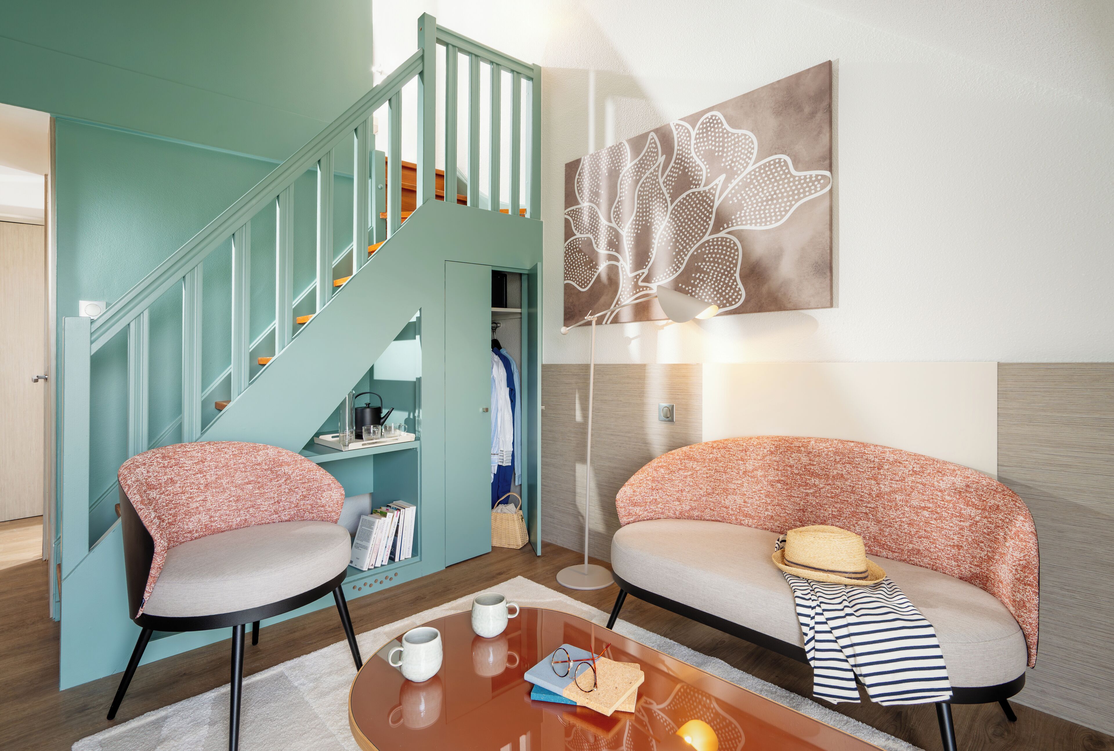 Una sala de estar moderna con paredes azul verdosas, una escalera, un sofá, una mesa de centro y una obra de arte en la pared.
