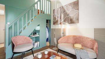 Una sala de estar moderna con paredes azul verdosas, una escalera, un sofá, una mesa de centro y una obra de arte en la pared.