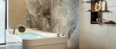Un baño moderno con pared de piedra, una bañera y estantes minimalistas con objetos decorativos.