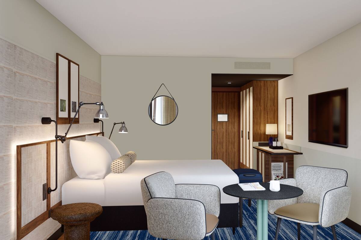 A hotel room with a bed, two armchairs, a small table, a lamp, and a mirror.