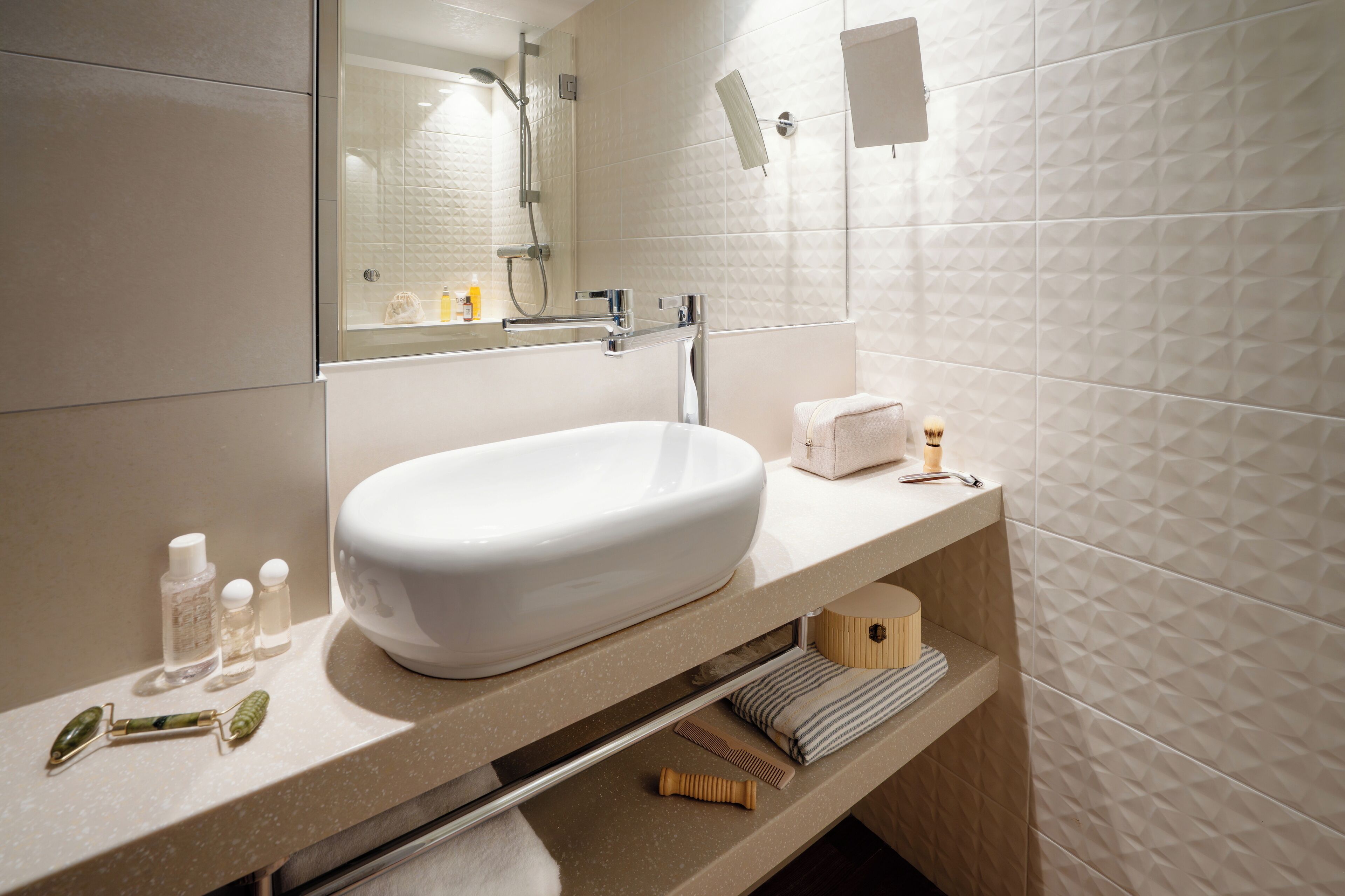 Une salle de bain moderne avec un grand lavabo blanc, un miroir et une douche. On y trouve des articles de toilette sur le comptoir, notamment un flacon de lotion, un rasoir et un peigne.