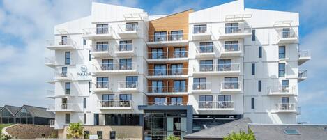 A modern multi-story hotel with balconies, a central entrance, and a stone facade.
