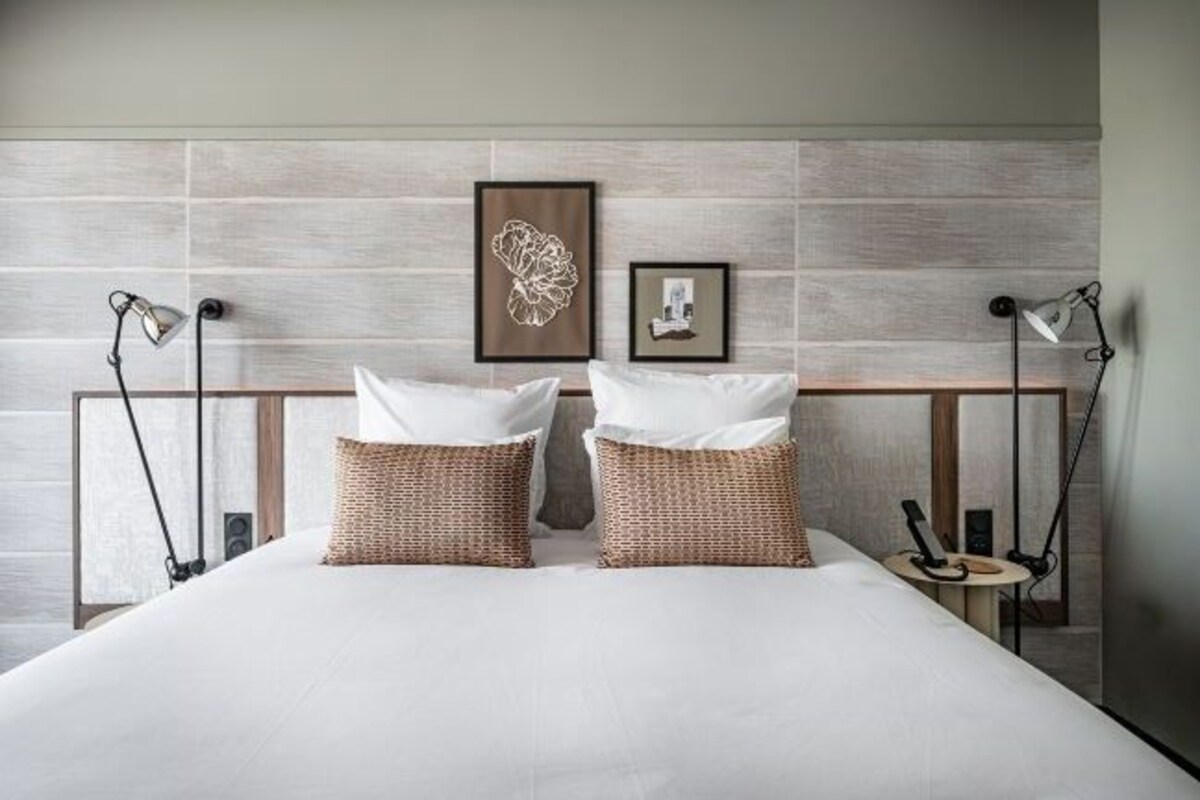A hotel room with a large bed, two bedside lamps, a small table, and two wall-mounted picture frames.