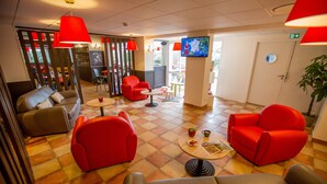 A hotel lobby with red chairs, a grey sofa, a TV on the wall, and a plant. - ibis Cherbourg La Glacerie (Cherbourg-en-Cotentin)