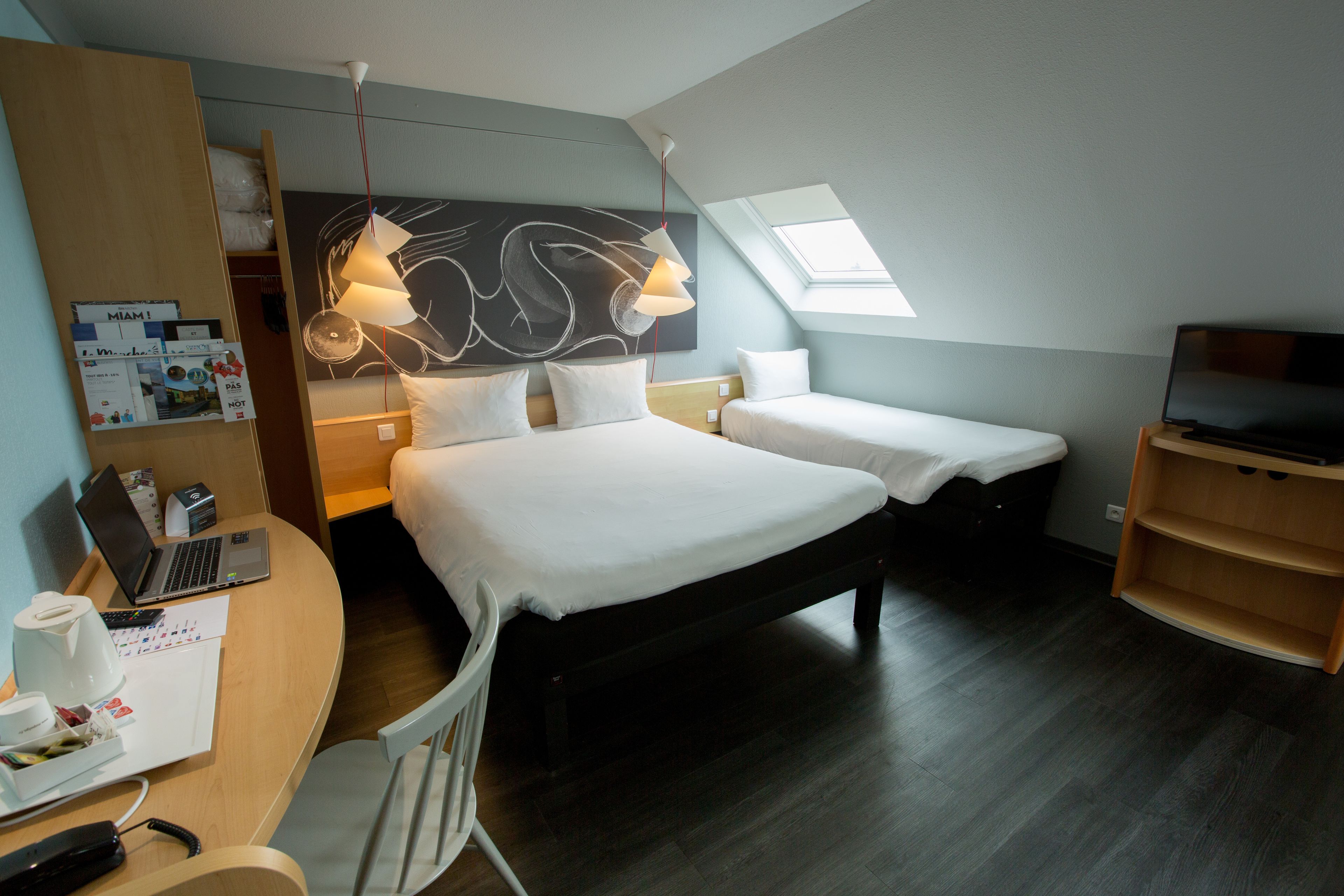 Ein Hotelzimmer mit einem Bett, einem Schreibtisch mit Laptop, einem Fernseher und einem Oberlicht.