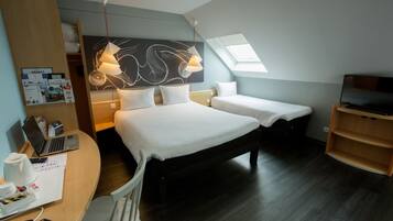 A hotel room with a bed, a desk with a laptop, a TV, and a skylight.