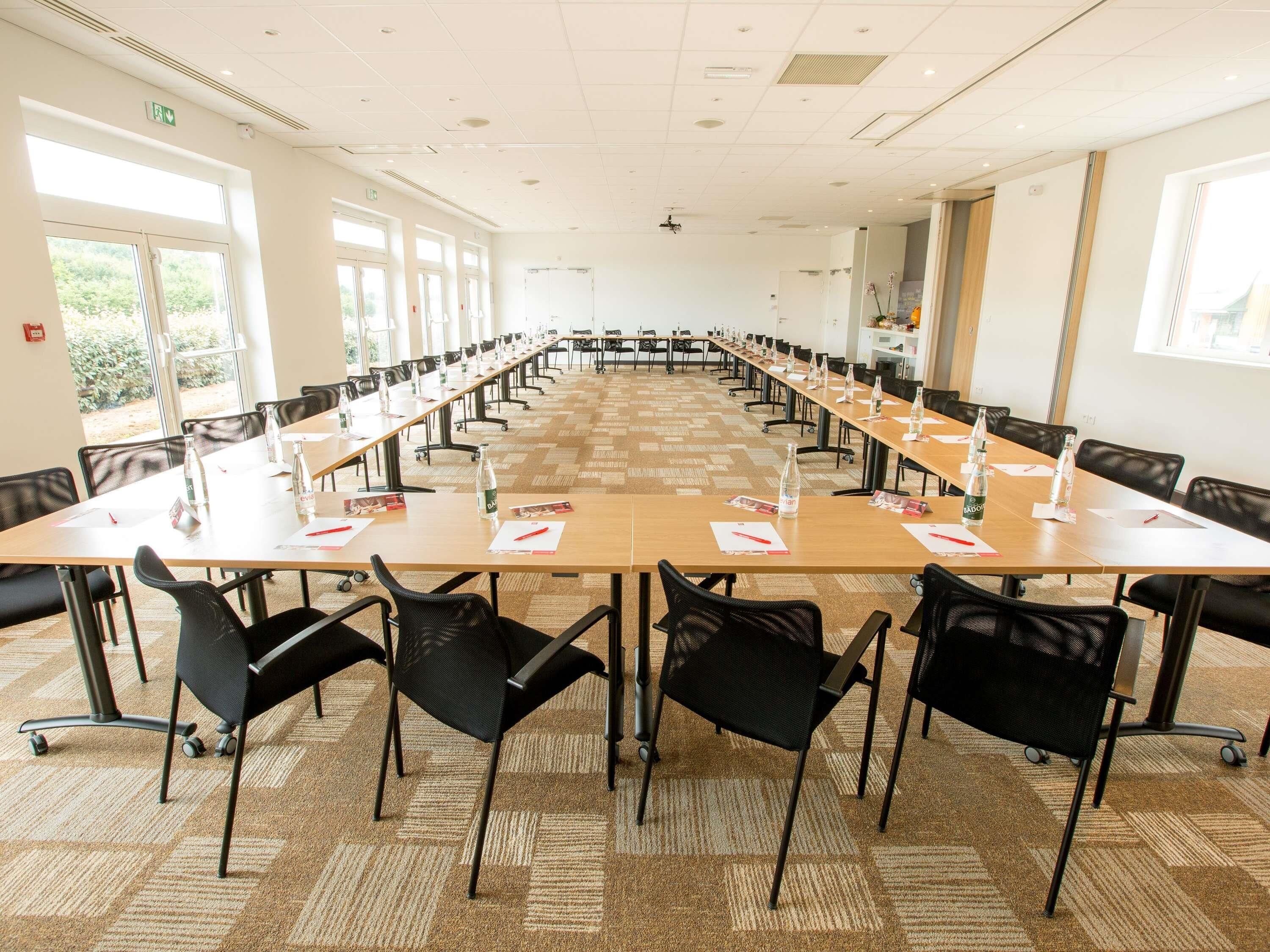 Un salón de conferencias con mesas largas, sillas y botellas de agua.