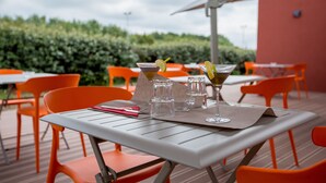 Un espace extérieur aménagé pour les repas, avec des tables et des chaises, un ciel dégagé et une haie en arrière-plan.