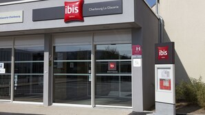 L’extérieur de l’hôtel ibis Cherbourg La Glacerie, avec son entrée en verre et son panneau indicateur.
