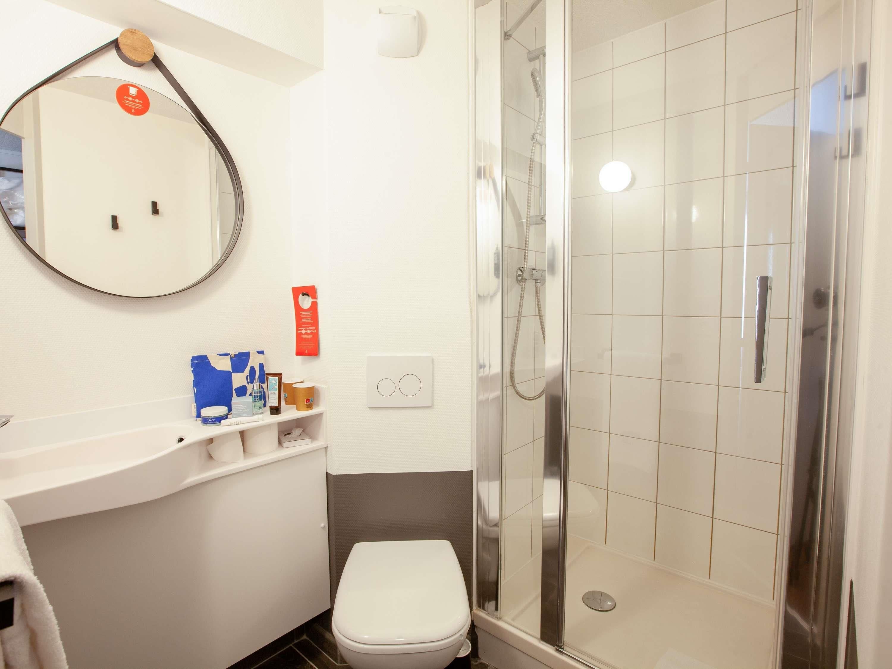 Un baño moderno con un lavabo blanco, un espejo, cabina de ducha y artículos de aseo en la encimera.
