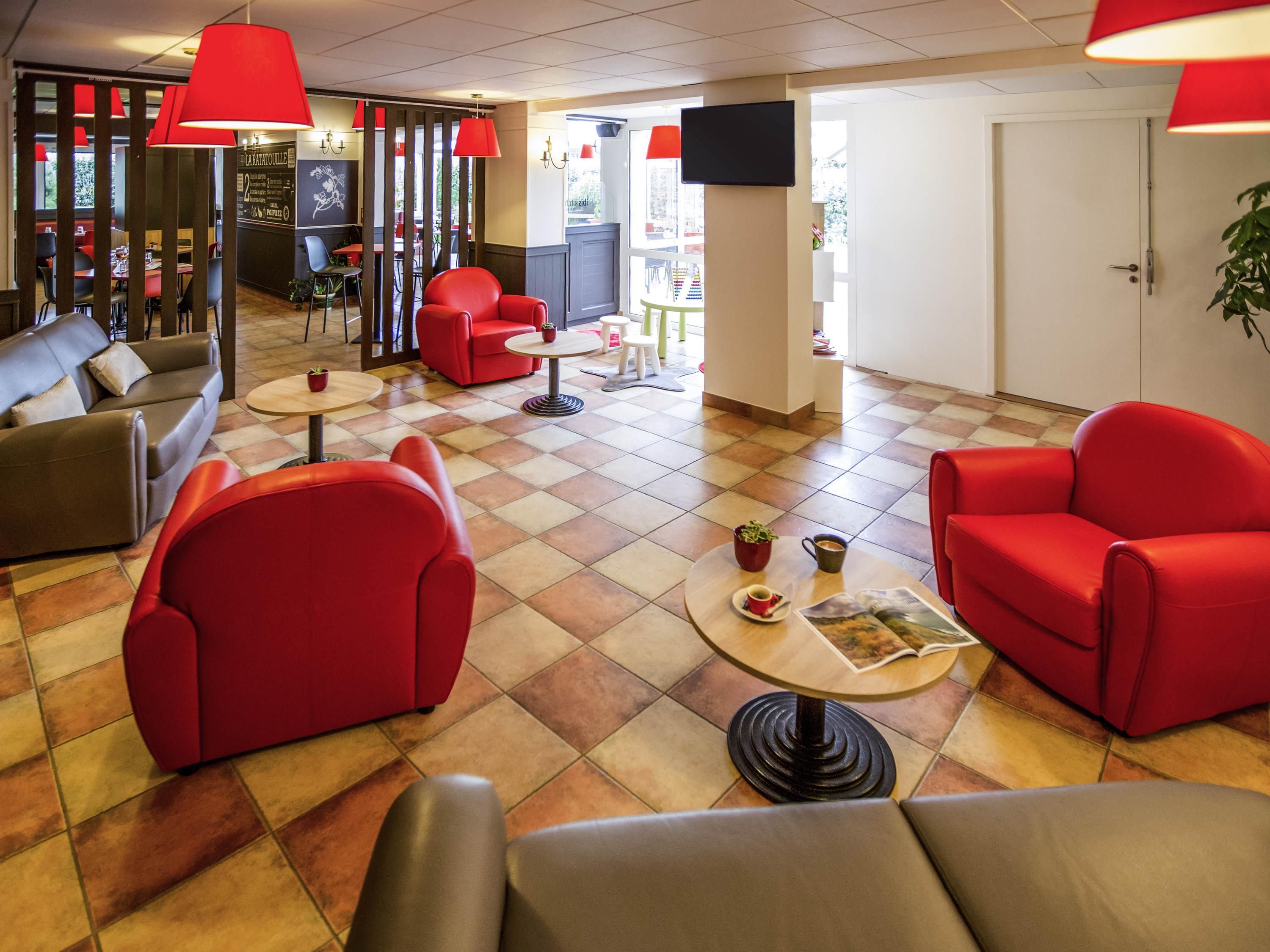 Un vestíbulo de hotel con asientos rojos, un televisor en la pared y piso de baldosas.