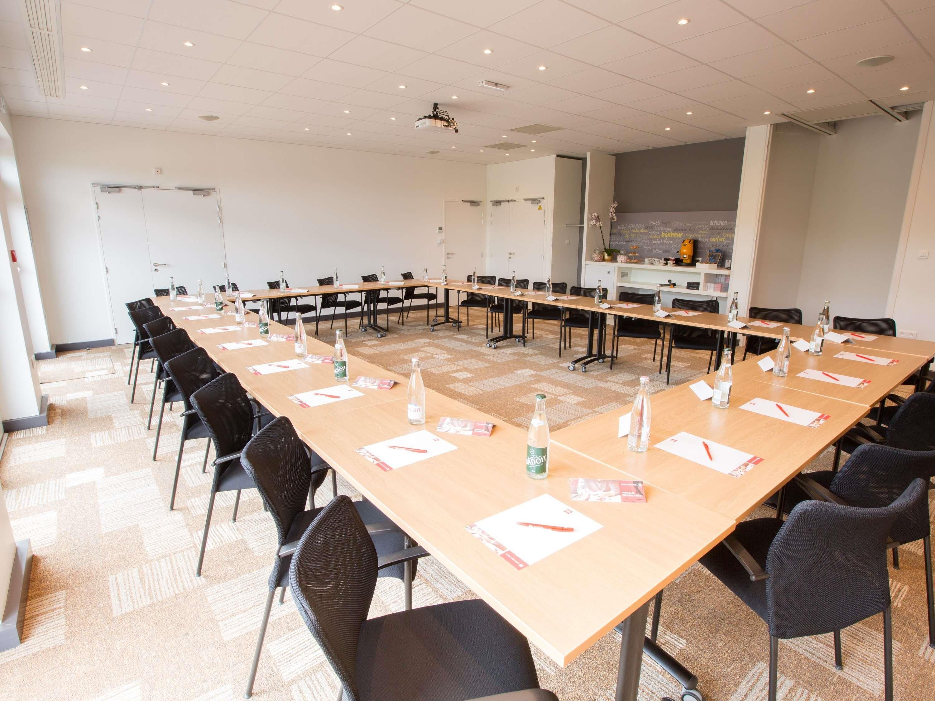 Une salle de conférence équipée de longues tables, de chaises et d’un projecteur.
