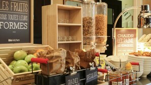 Una encimera de cocina con recipientes etiquetados de cereales, una exhibición de manzanas verdes y un letrero que anuncia panadería y pastelería.