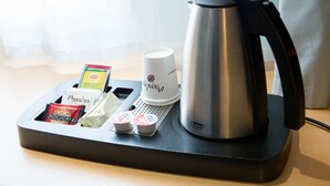 Une machine à café, une tasse, un plateau avec un croissant, un muffin et un sachet de crème liquide.