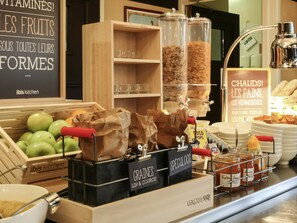 Una encimera de cocina con recipientes etiquetados de cereales, una exhibición de manzanas verdes y un letrero que anuncia panadería y pastelería.