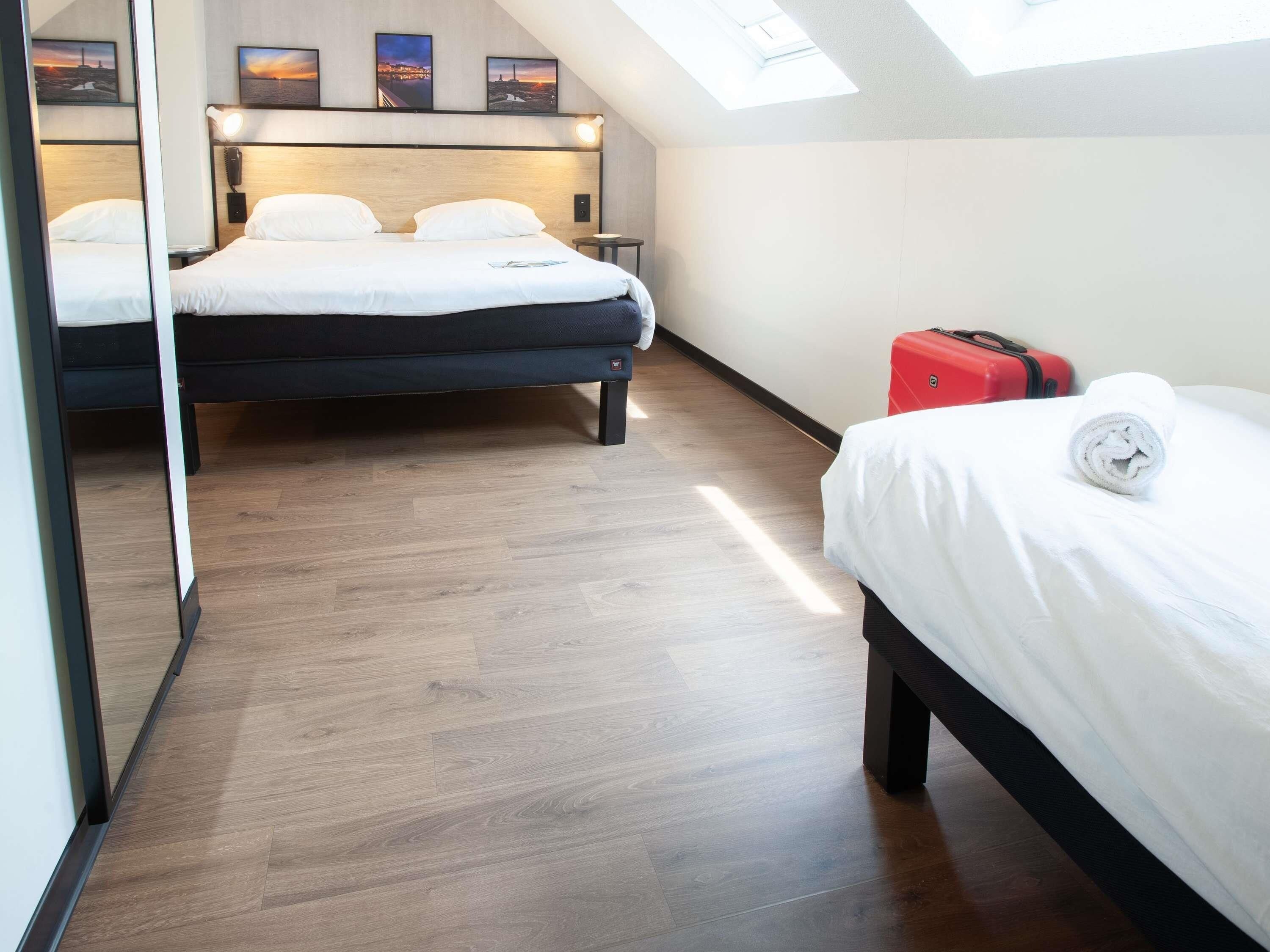 Een hotelkamer met twee bedden, een dakraam, houten vloeren en een rode koffer.