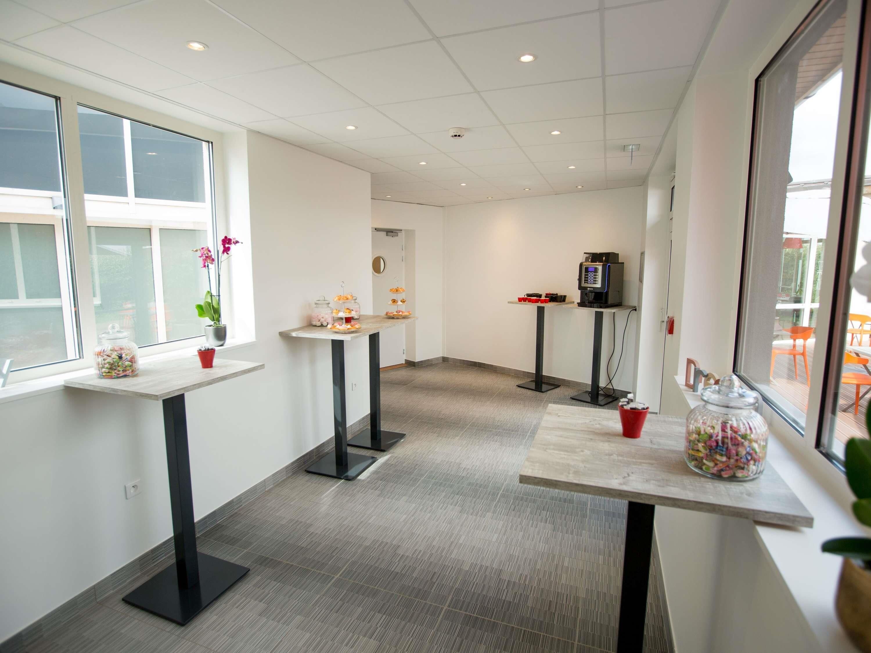 A modern hotel room with a large window, a small table with a plant, a coffee machine, and a glass jar of candies.