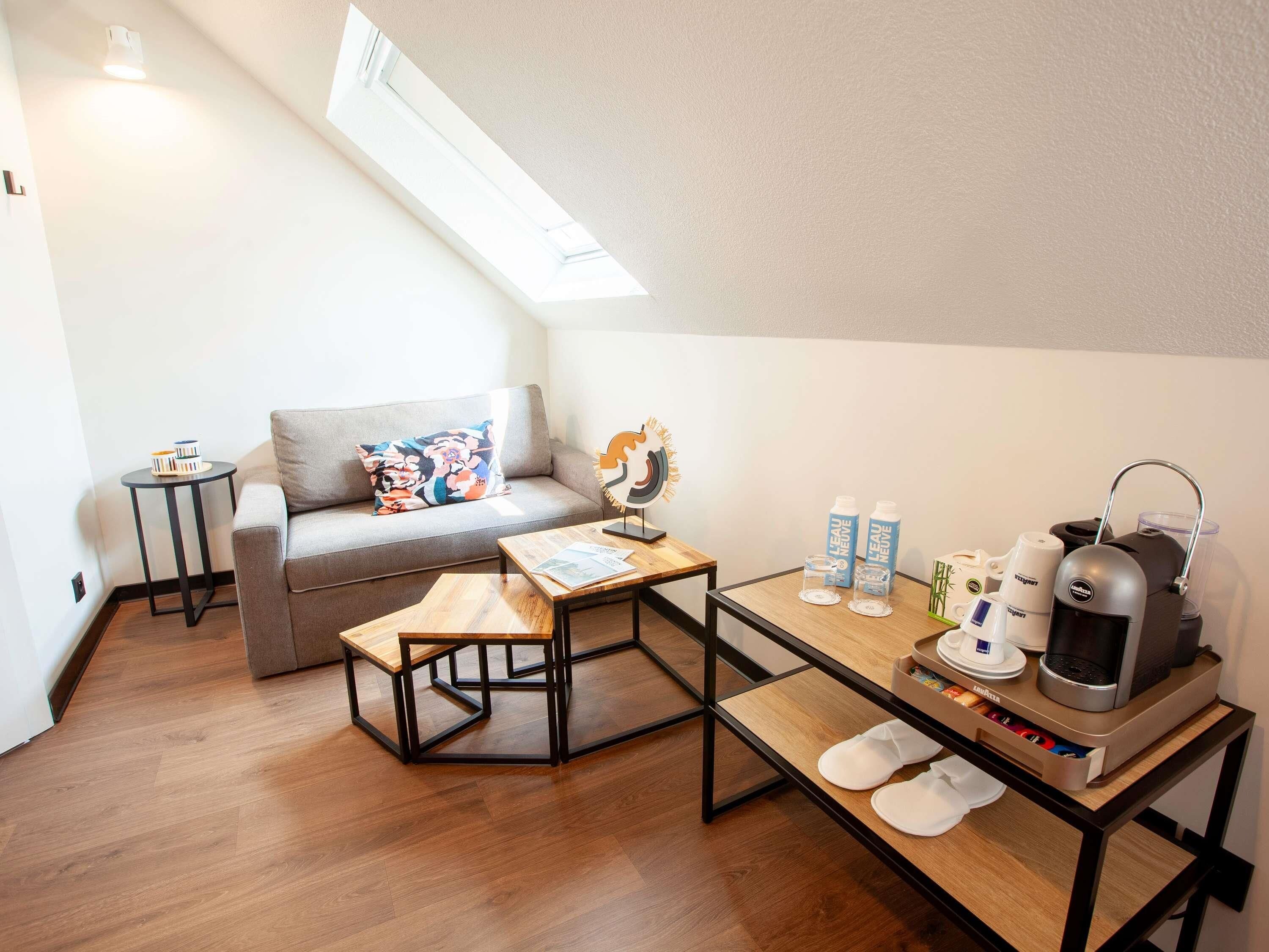 Un espace de vie moderne et compact comprenant un lit en mezzanine, un canapé, une table basse et un coin cuisine.