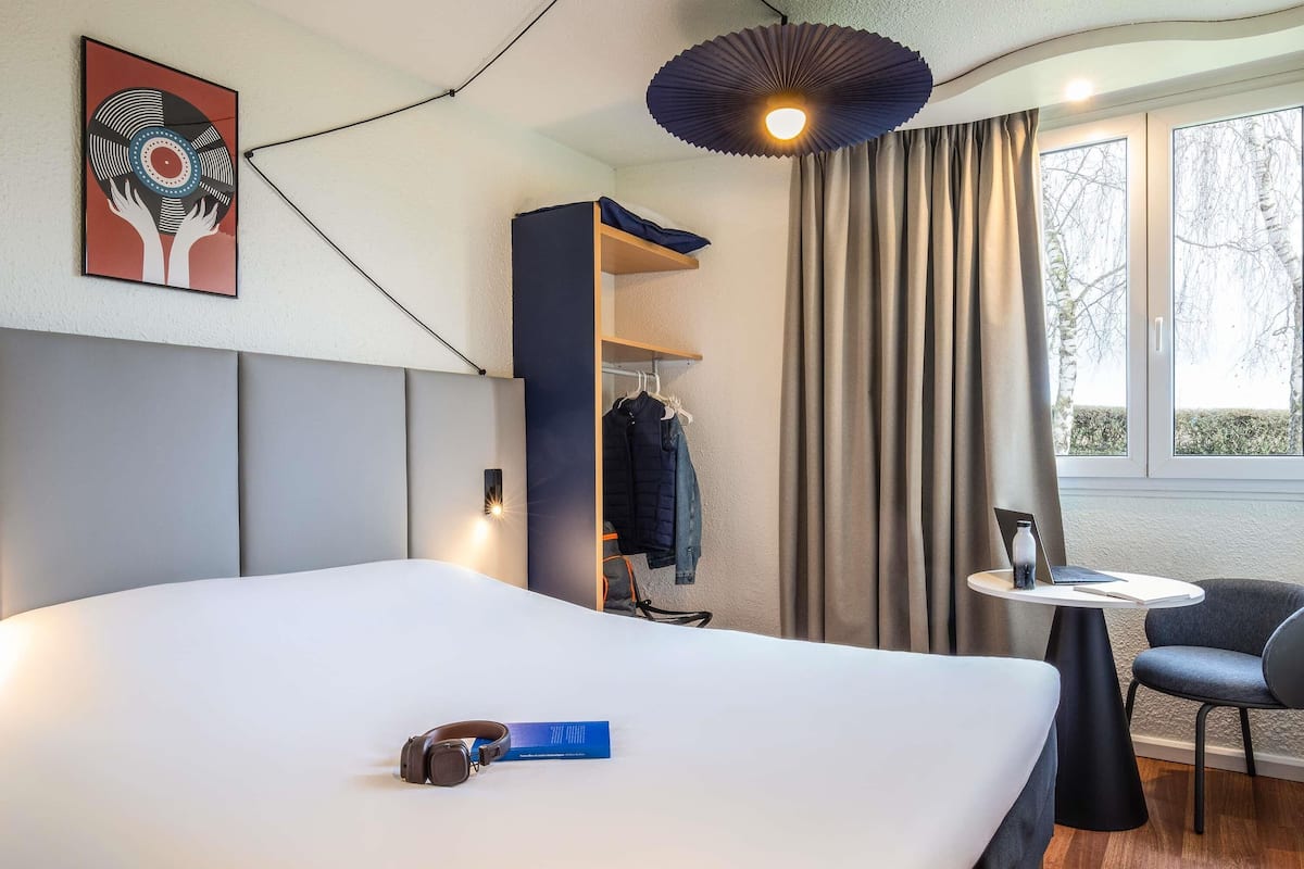 Een moderne hotelkamer met een groot bed, een bureau met een laptop, een stoel en een kledingkast.