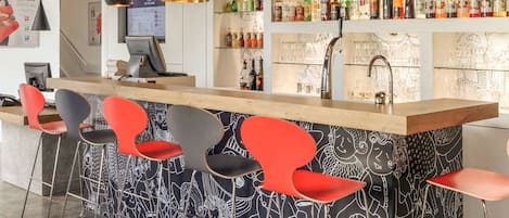 A bar area with a wooden counter, black and white patterned wall, red and grey bar stools, and a variety of liquor bottles.