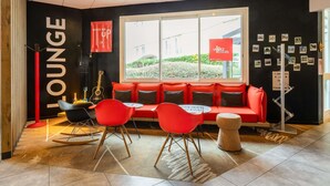 Un espace de détente moderne avec un canapé rouge, des fauteuils noirs et rouges, une guitare et une table en pierre.