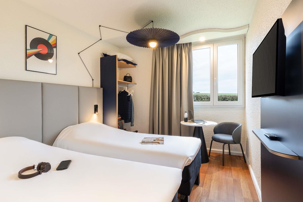 Hotelkamer met twee bedden, een bureau, een stoel, een televisie, een raam met uitzicht en een hanglamp.