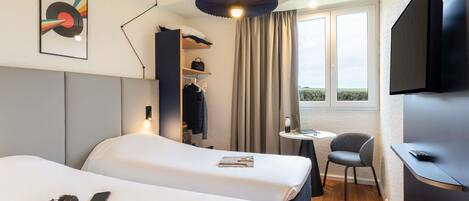 Habitación de hotel con dos camas, un escritorio, una silla, un televisor, una ventana con vistas y una lámpara colgante.