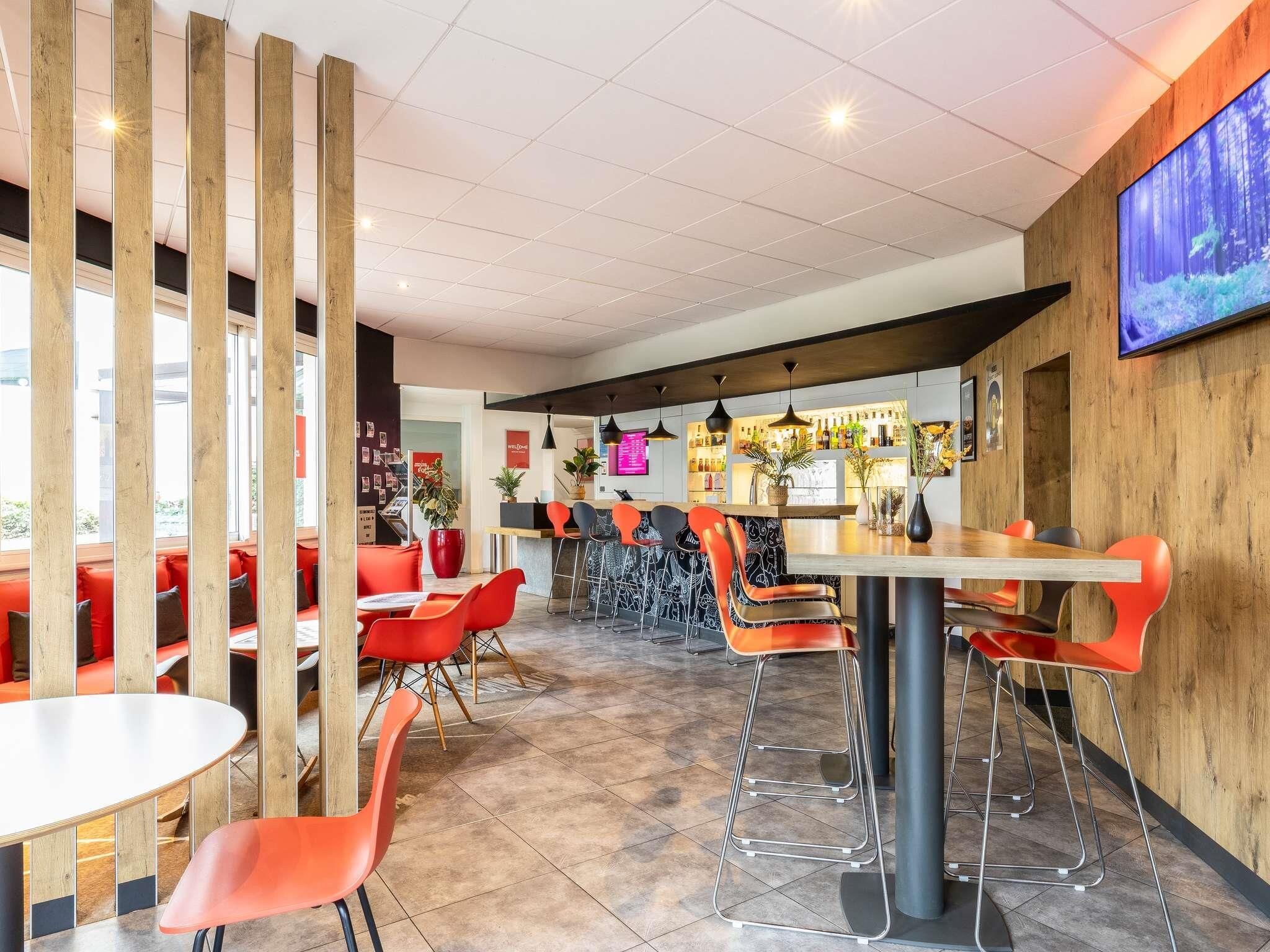 Un interior de restaurante moderno con mesas altas, sillas rojas y una zona de bar.