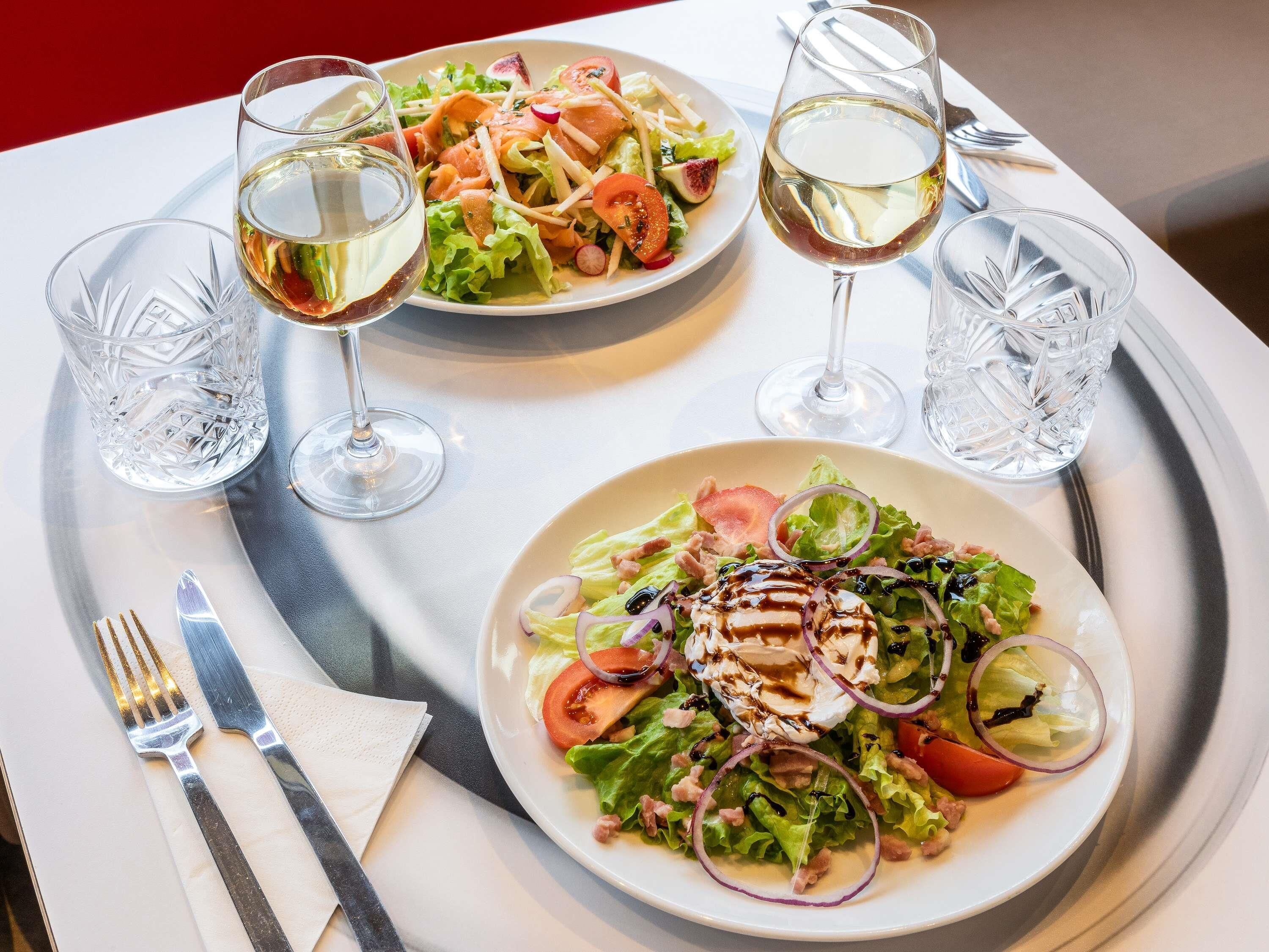A dining table with two plates of salad and two glasses of white wine.