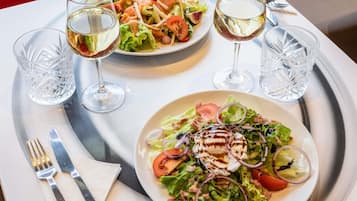 A dining table with two plates of salad and two glasses of white wine.