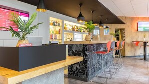 Un espace bar moderne avec un comptoir en bois, un mur à motifs noir et blanc et de nombreuses suspensions lumineuses.
