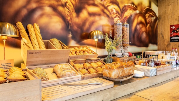 Une vitrine de boulangerie présentant diverses sortes de pains et de viennoiseries, notamment des baguettes et des croissants, dans des boîtes en bois étiquetées « Cuisine Ibis ».