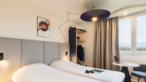 Une chambre d’hôtel moderne dotée d’un grand lit, d’un bureau avec un ordinateur portable, d’une chaise et offrant une vue sur l’extérieur.
