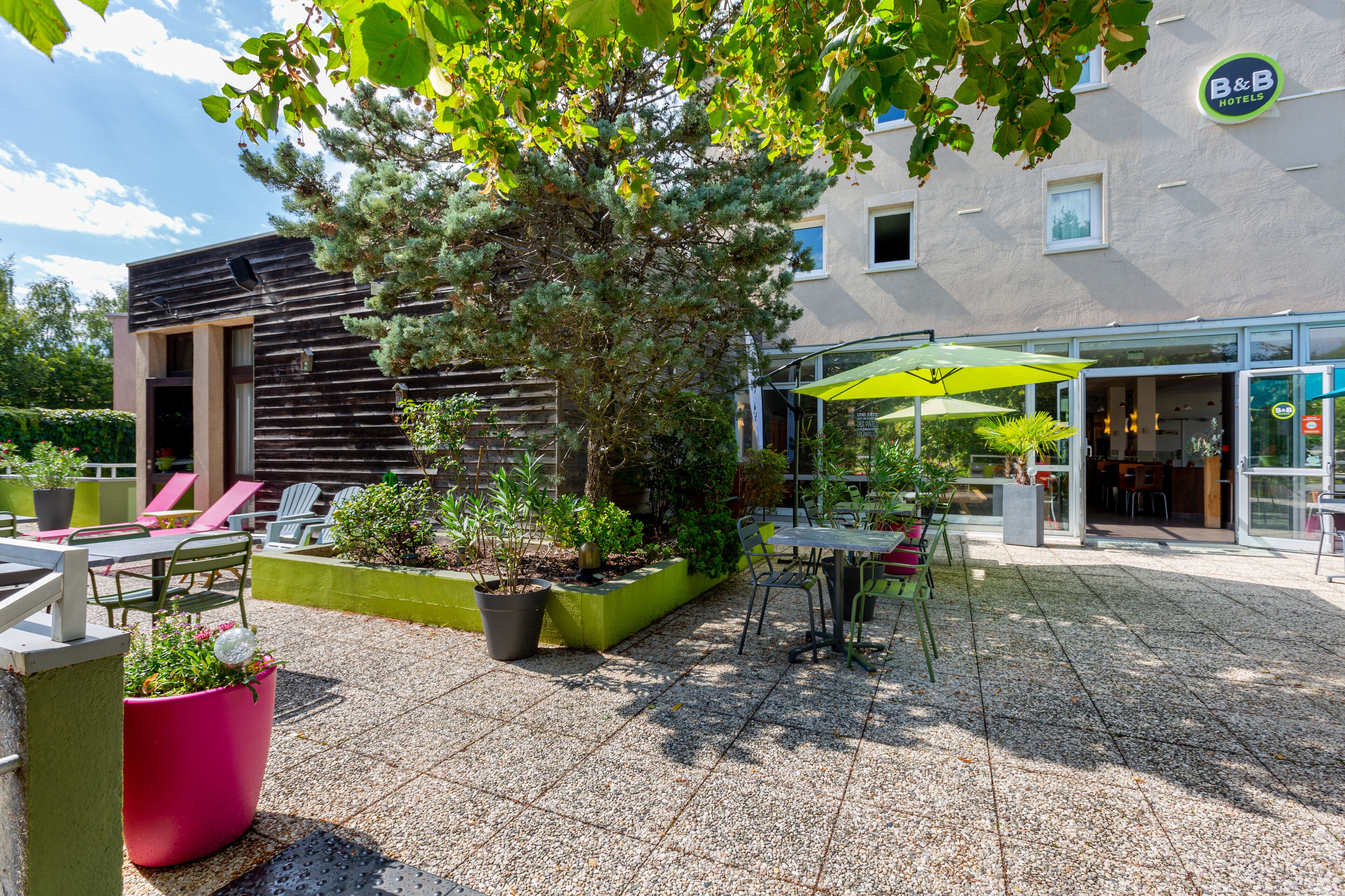 A hotel courtyard with outdoor seating, potted plants, and a building with a sign reading "B&B Hotels".