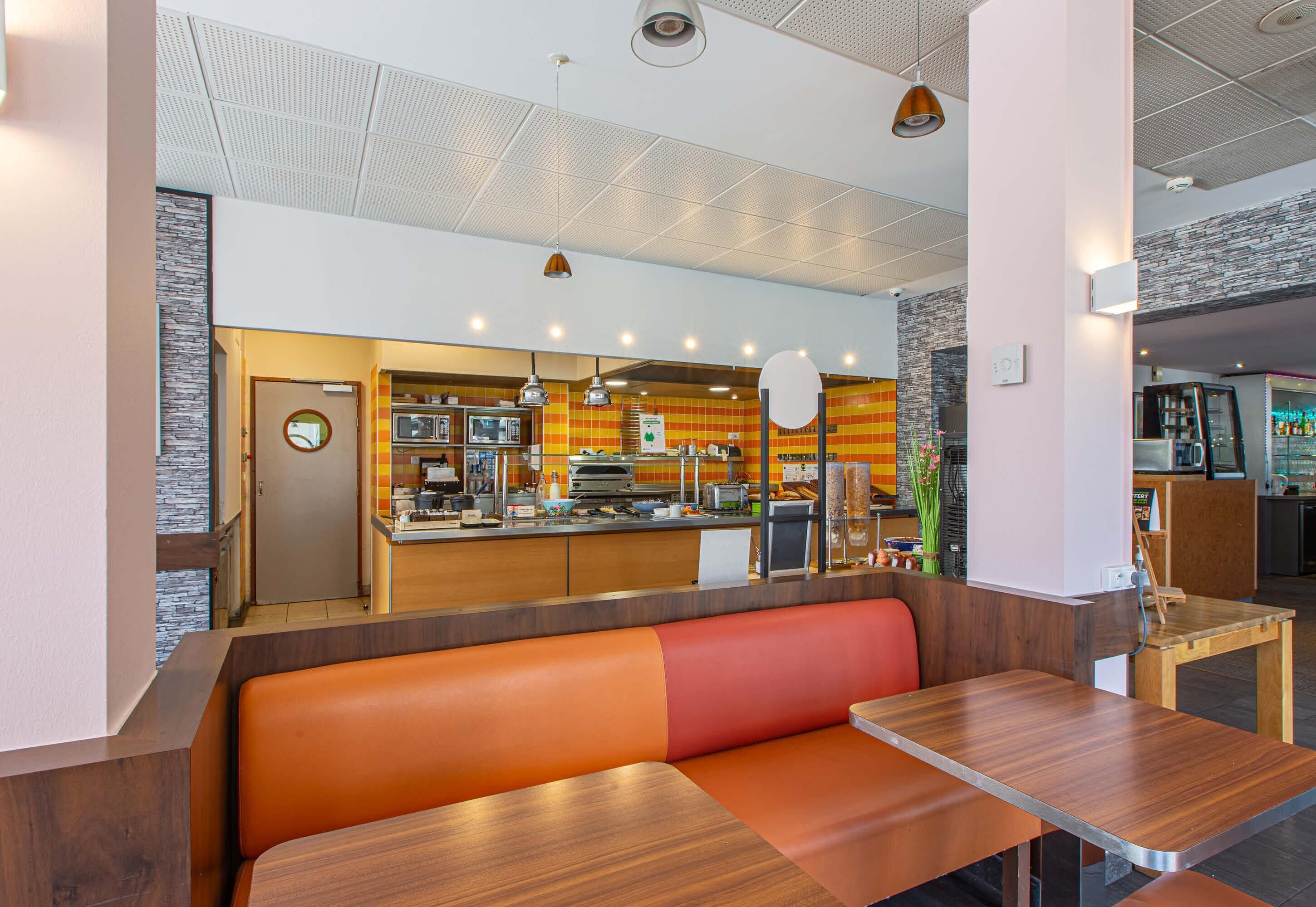 A restaurant with a counter, seating area, and kitchen in the background.