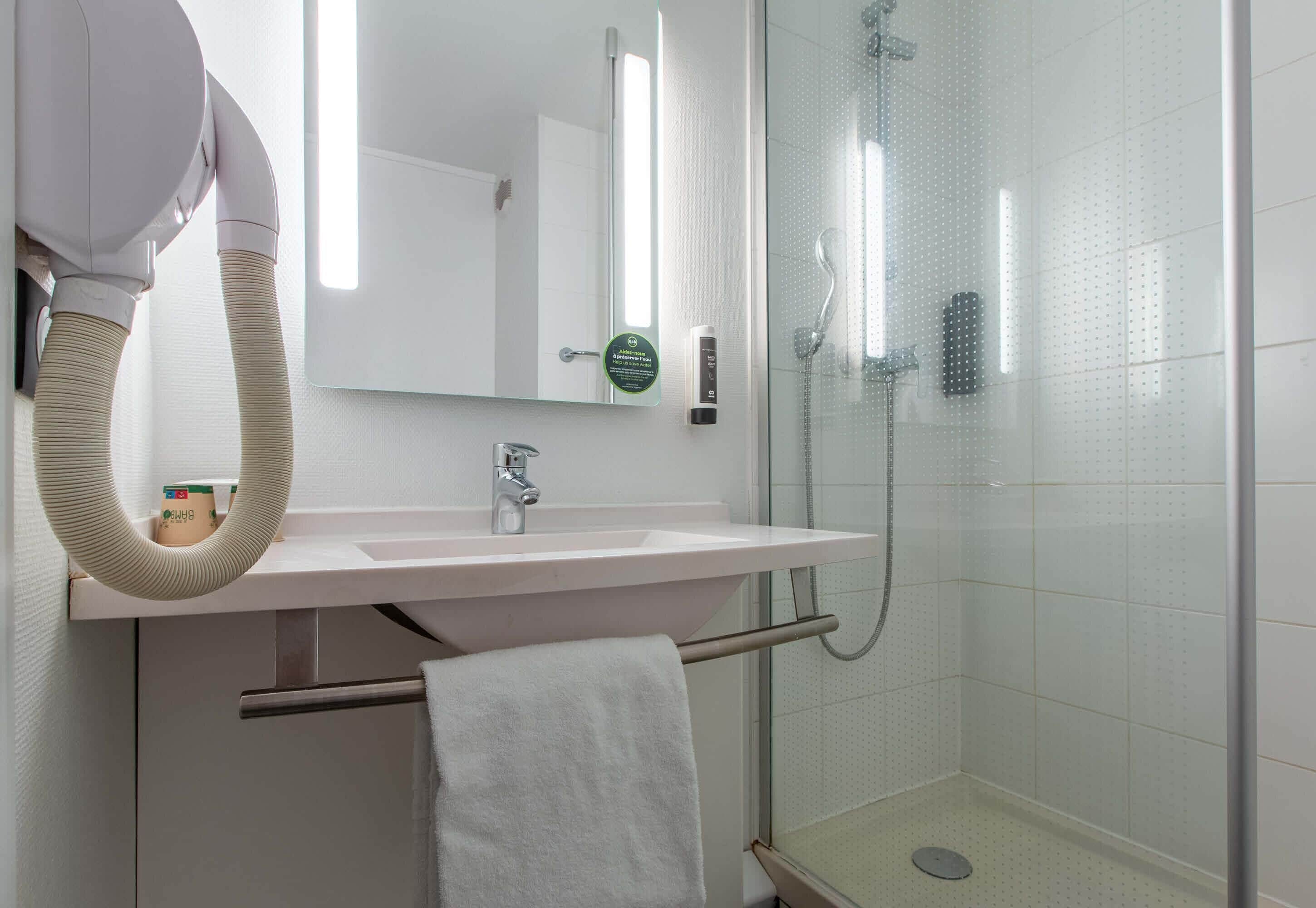A bathroom with a sink, mirror, towel rack, and a glass shower enclosure.