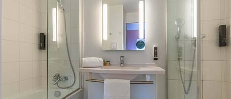 Un baño moderno con ducha envuelta en vidrio, un lavabo blanco y un espejo sobre él.
